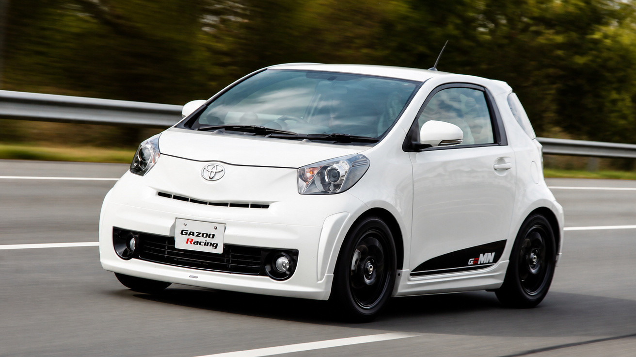 Carro compacto branco Toyota a circular rapidamente numa estrada com proteção metálica ao fundo.