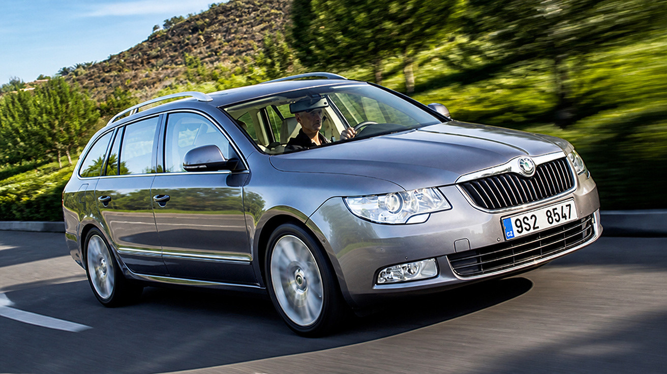 Automóvel Skoda Superb break cinzento a circular numa estrada com vegetação ao fundo.