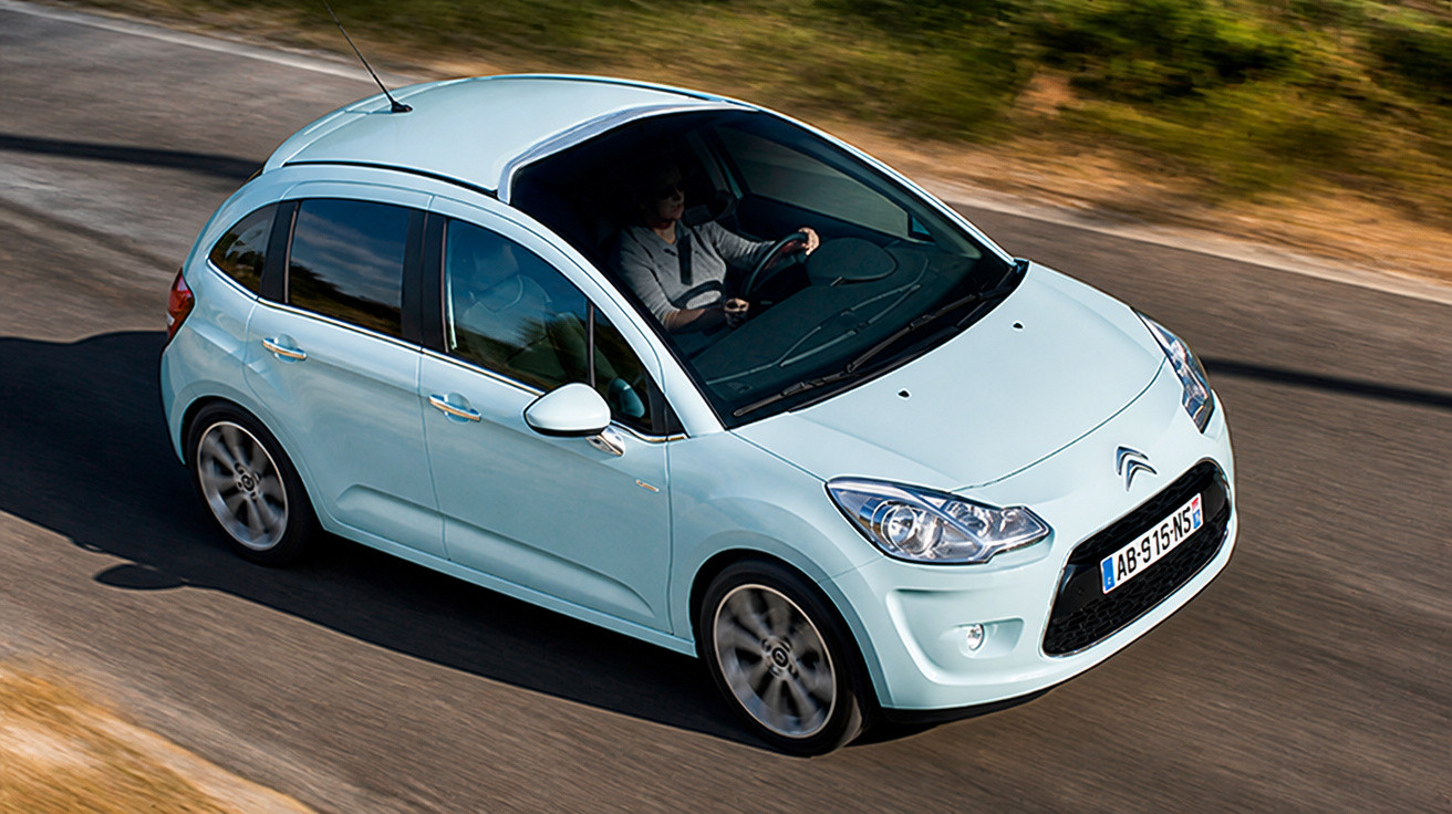 Carro Citroën azul claro a circular numa estrada com um condutor ao volante.