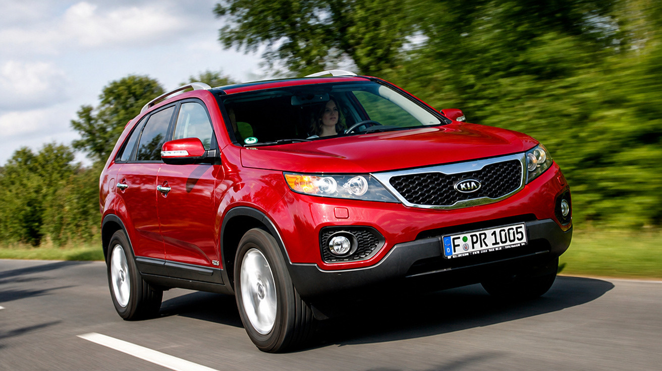 Carro SUV vermelho Kia a circular numa estrada rodeada de vegetação verde.