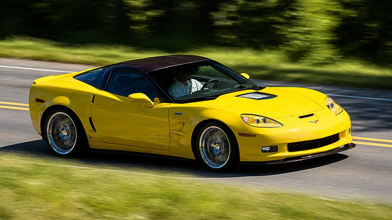 Carro desportivo amarelo a circular numa estrada rodeada de vegetação verde.