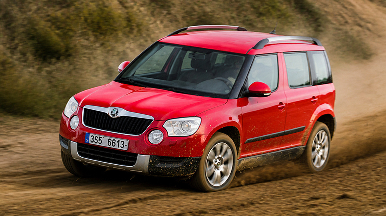 Carro SUV vermelho a circular numa estrada de terra, com pó e lama nas rodas e laterais.