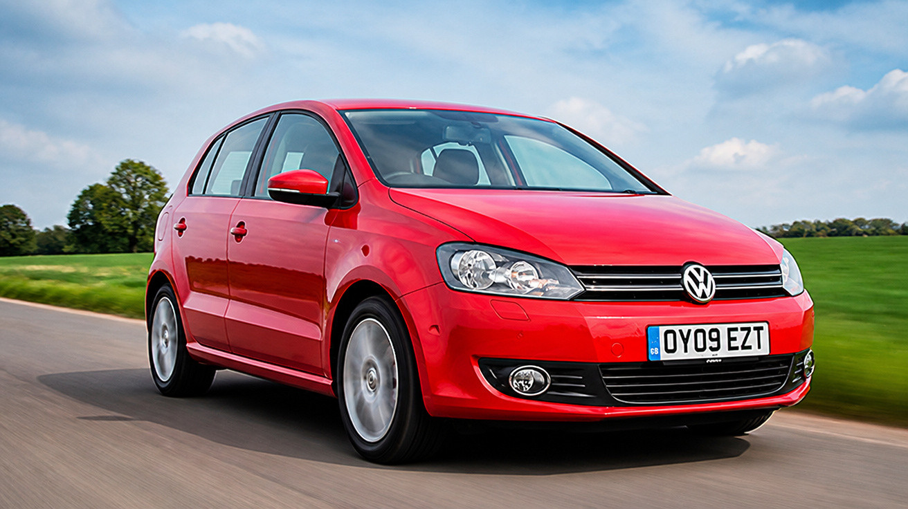 Carro vermelho Volkswagen em movimento numa estrada rural com céu parcialmente nublado.