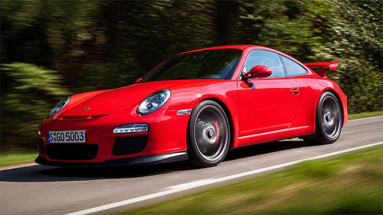 Carro desportivo vermelho Porsche a alta velocidade numa estrada rodeada de árvores verdes.