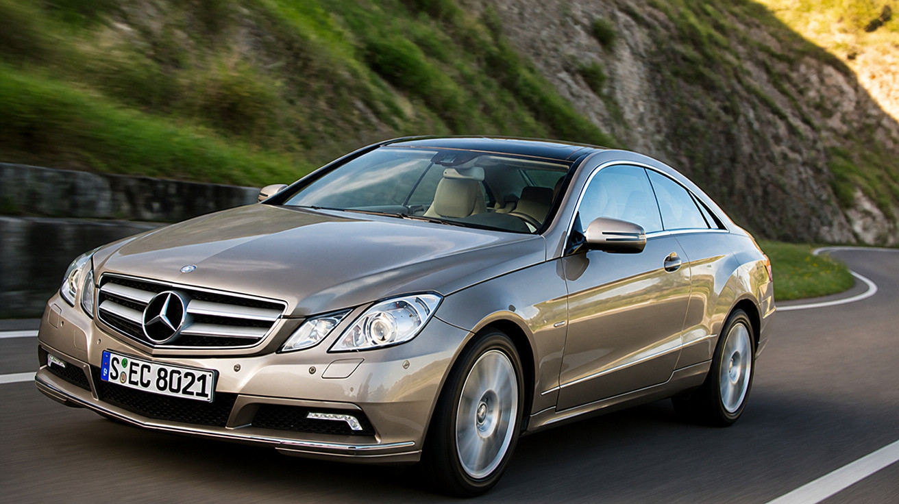 Carro Mercedes-Benz cinza a circular numa estrada curva entre colinas com vegetação.