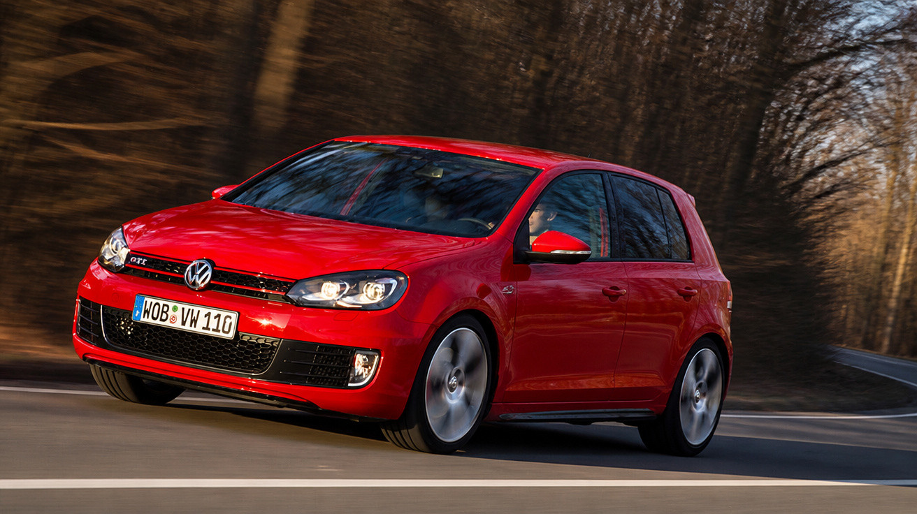 Carro desportivo Volkswagen Golf GTI vermelho a circular numa estrada sinuosa com árvores ao fundo.