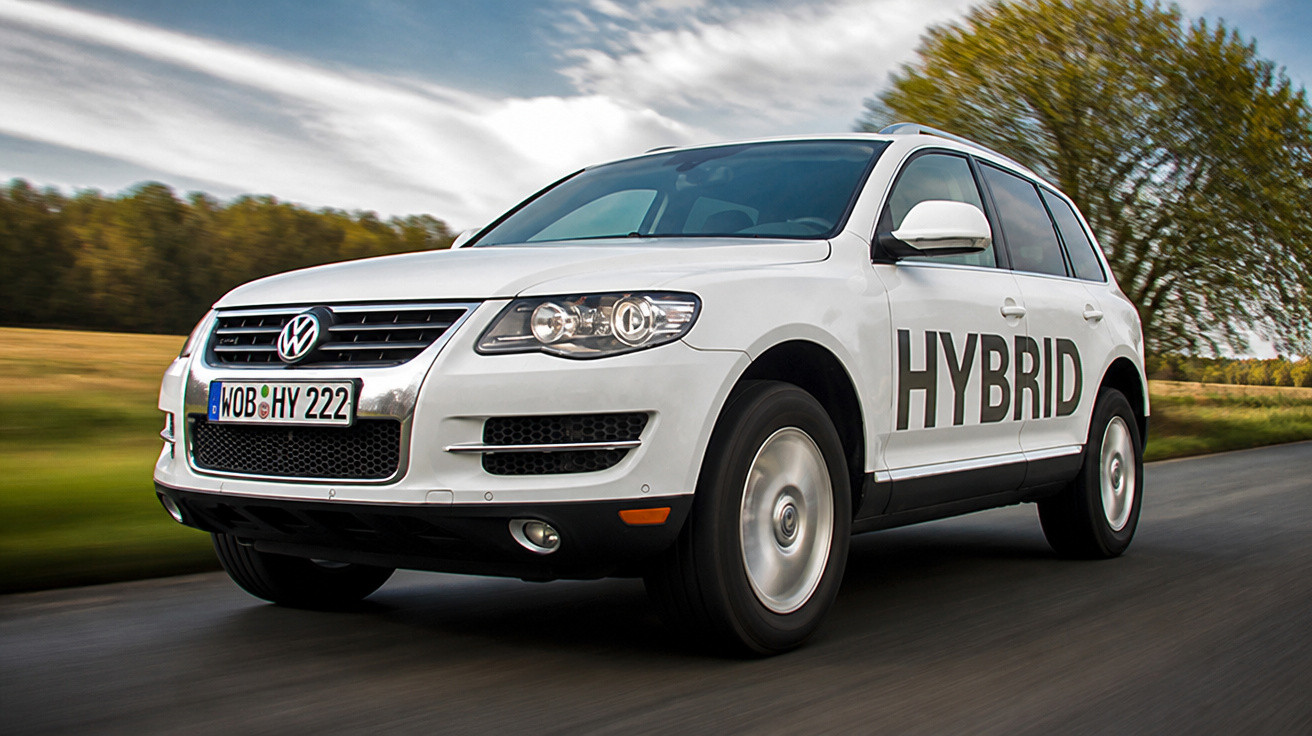 Carro SUV híbrido branco em movimento numa estrada rodeada de árvores e relva verde.