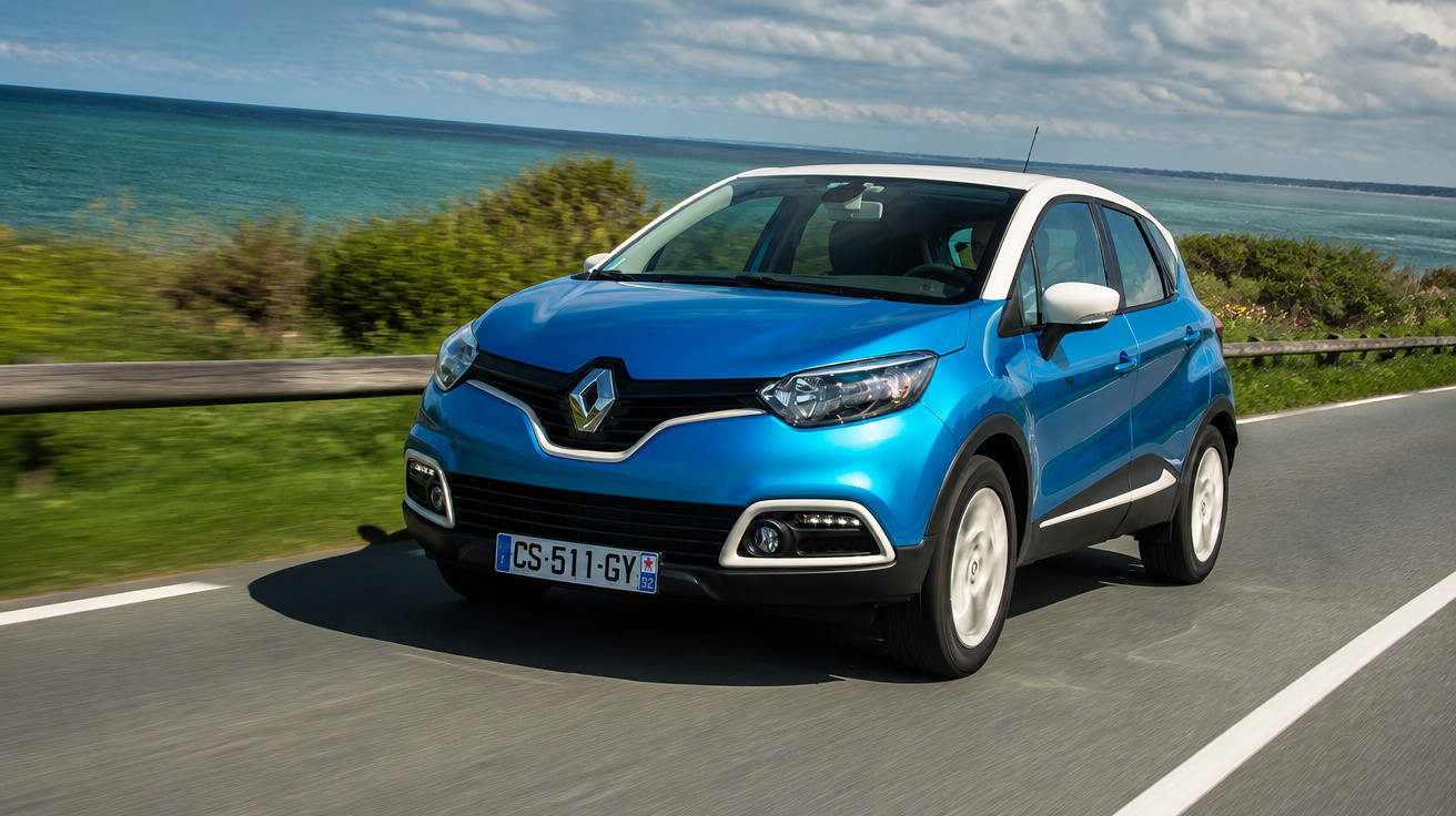 Carro azul Renault a circular numa estrada costeira junto ao mar em dia ensolarado.