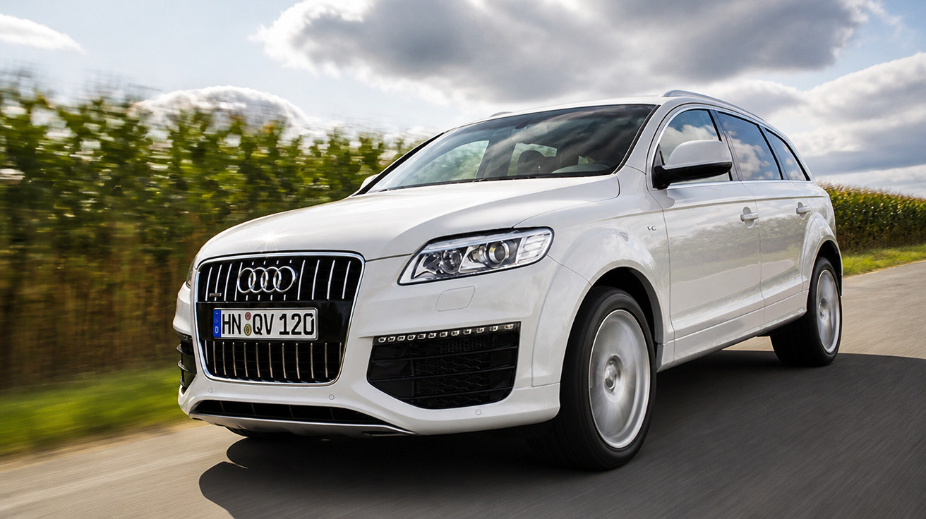 Audi Q7 branco a circular numa estrada rural sob céu parcialmente nublado.