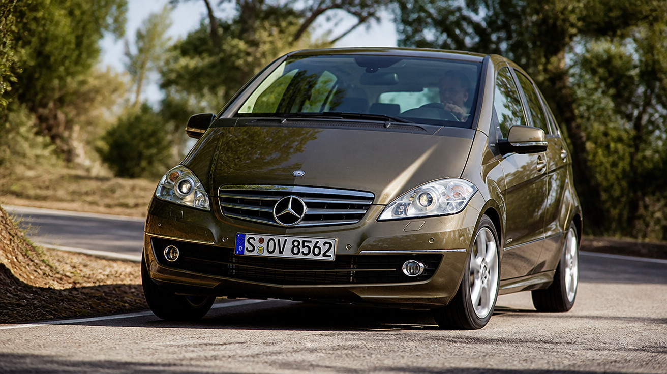 Carro Mercedes-Benz castanho conduzido numa estrada com árvores ao fundo.