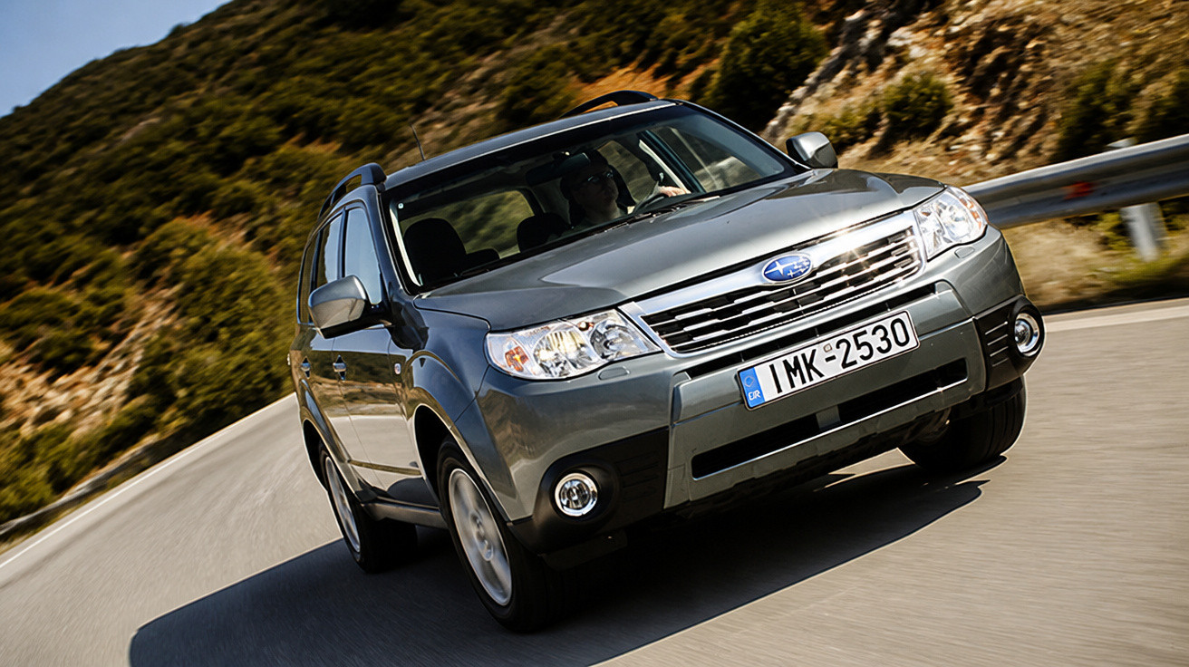 Carro Subaru cinzento a circular numa estrada sinuosa rodeada por vegetação e rochas
