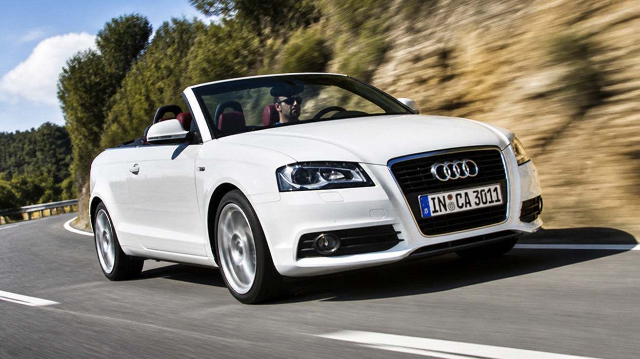 Carro descapotável Audi branco a circular numa estrada curva rodeada de vegetação e rochas.
