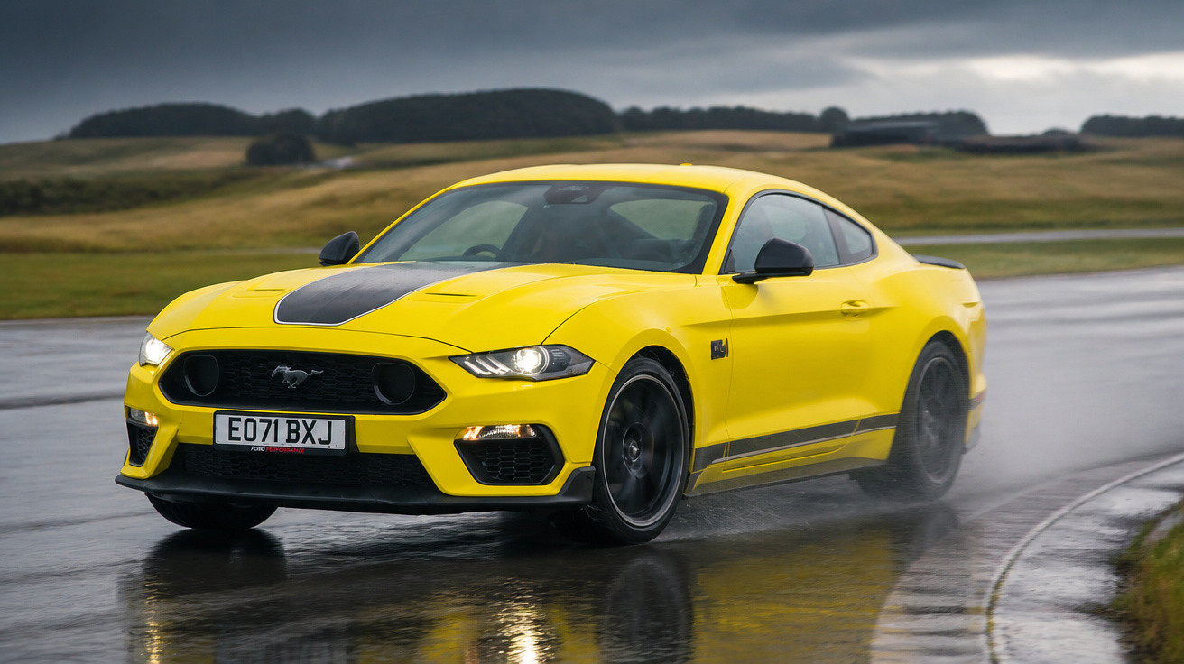 Carro desportivo amarelo Ford Mustang a acelerar numa estrada molhada num dia nublado.