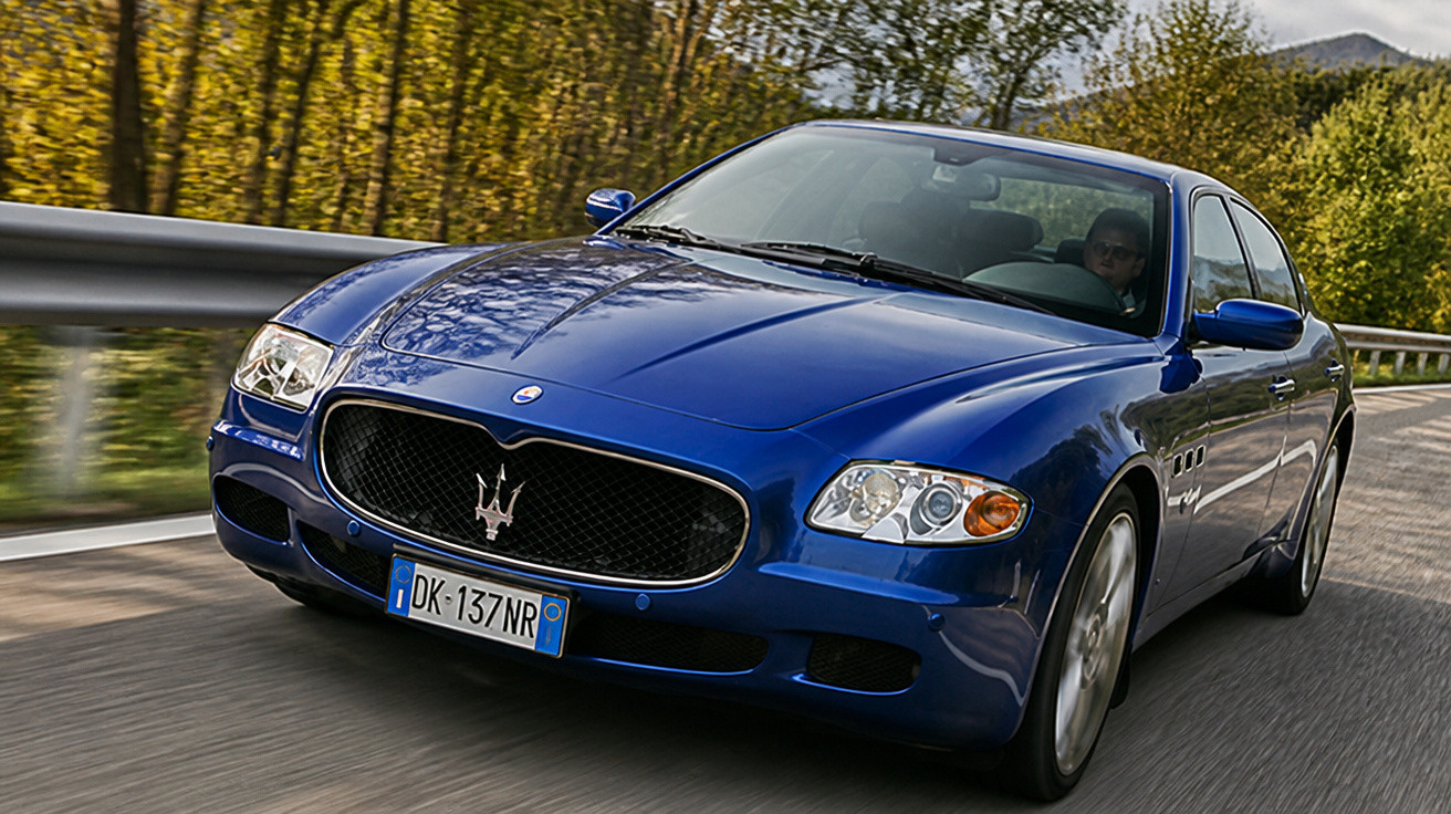 Carro desportivo azul Maserati a circular numa estrada com árvores ao fundo.