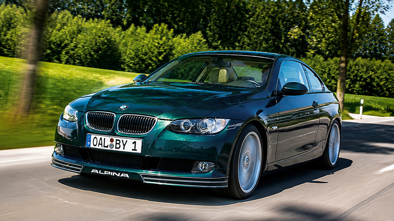 Carro verde BMW Alpina a circular numa estrada rodeada de árvores e relva verde.
