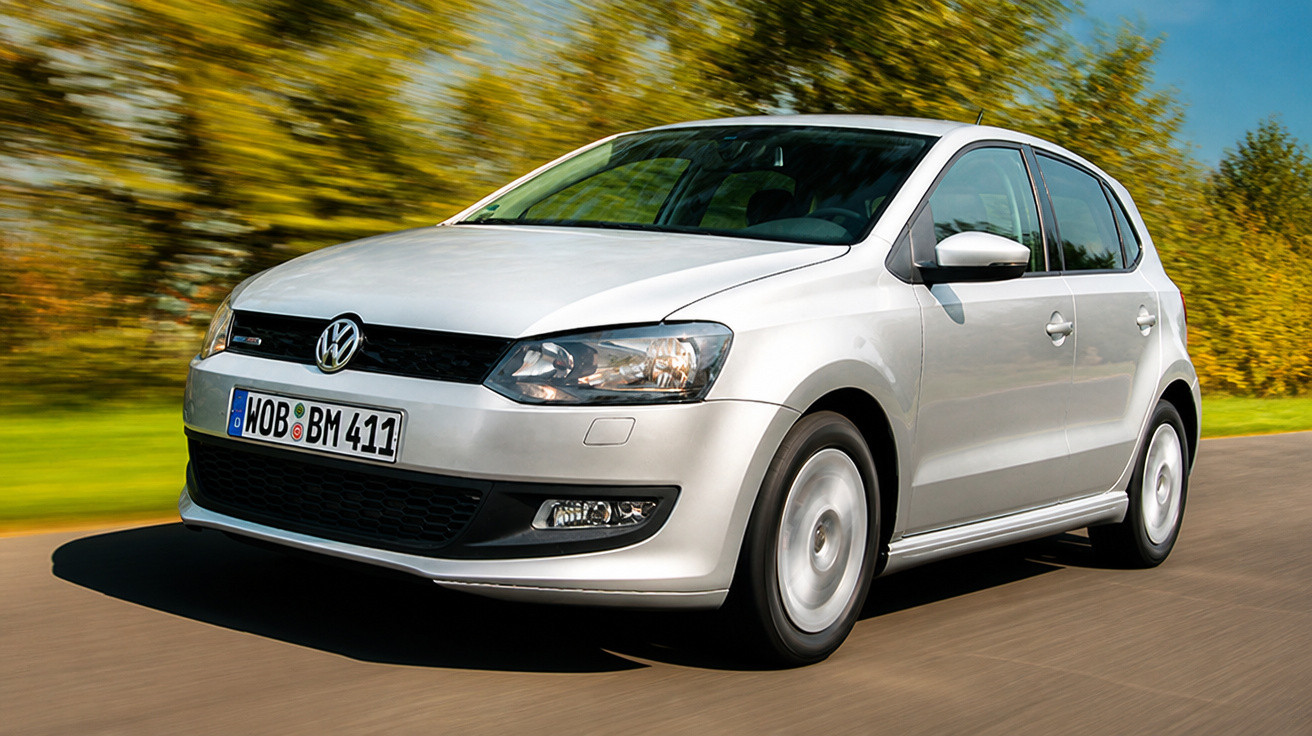 Carro Volkswagen branco a circular numa estrada rodeada de árvores com folhagem amarela.