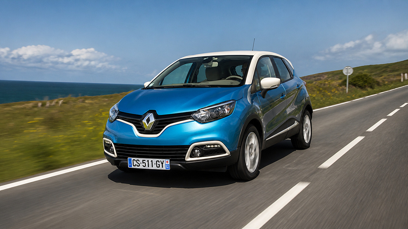 Carro azul Renault a circular numa estrada costeira sob céu azul com algumas nuvens.