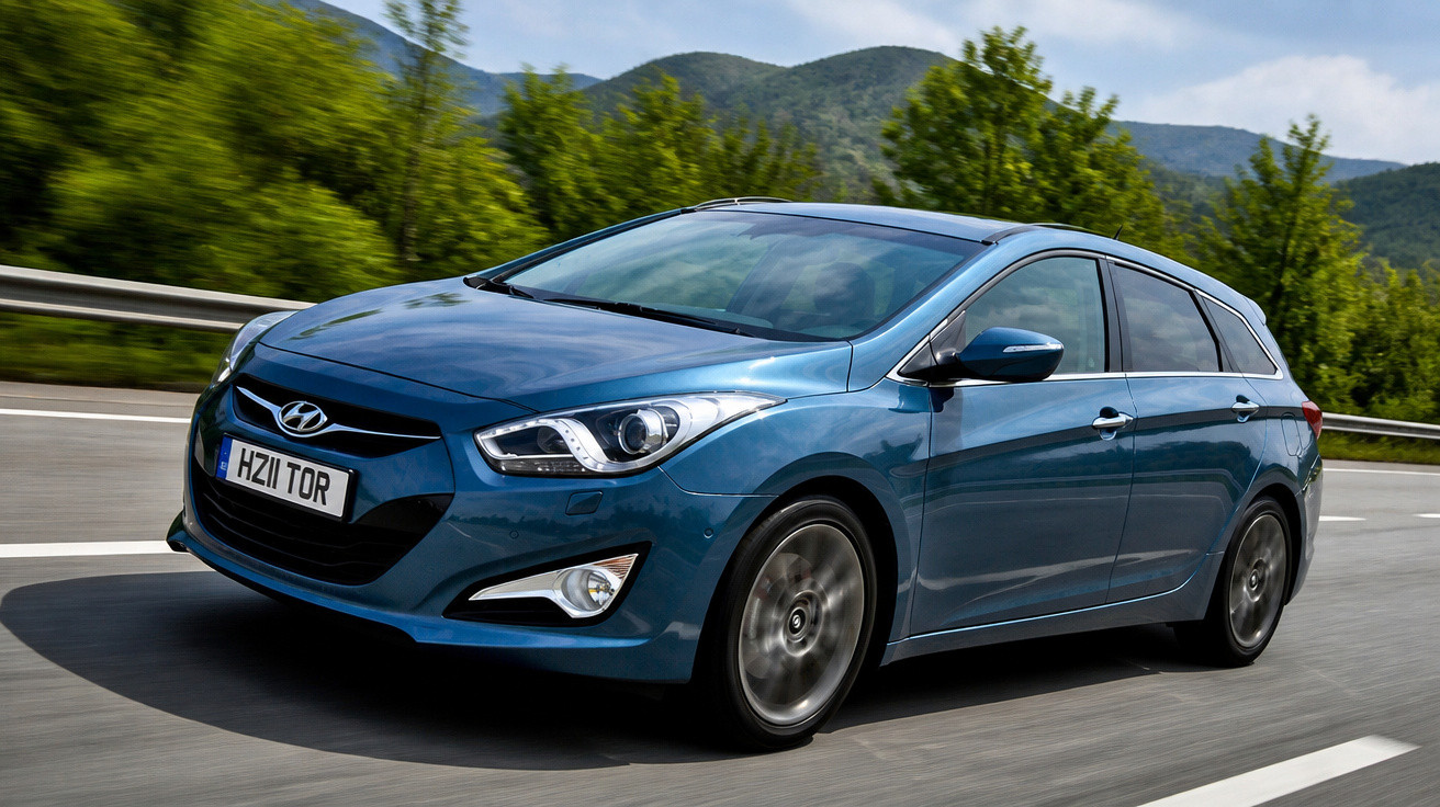 Carro Hyundai azul em movimento numa estrada ladeada por árvores e montanhas ao fundo.