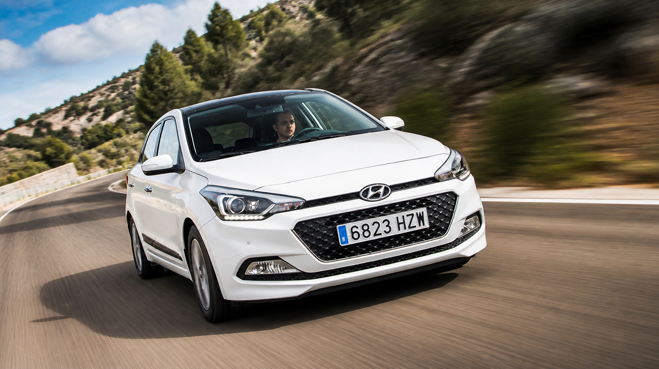 Carro branco Hyundai a circular numa estrada sinuosa em zona montanhosa com céu parcialmente nublado.