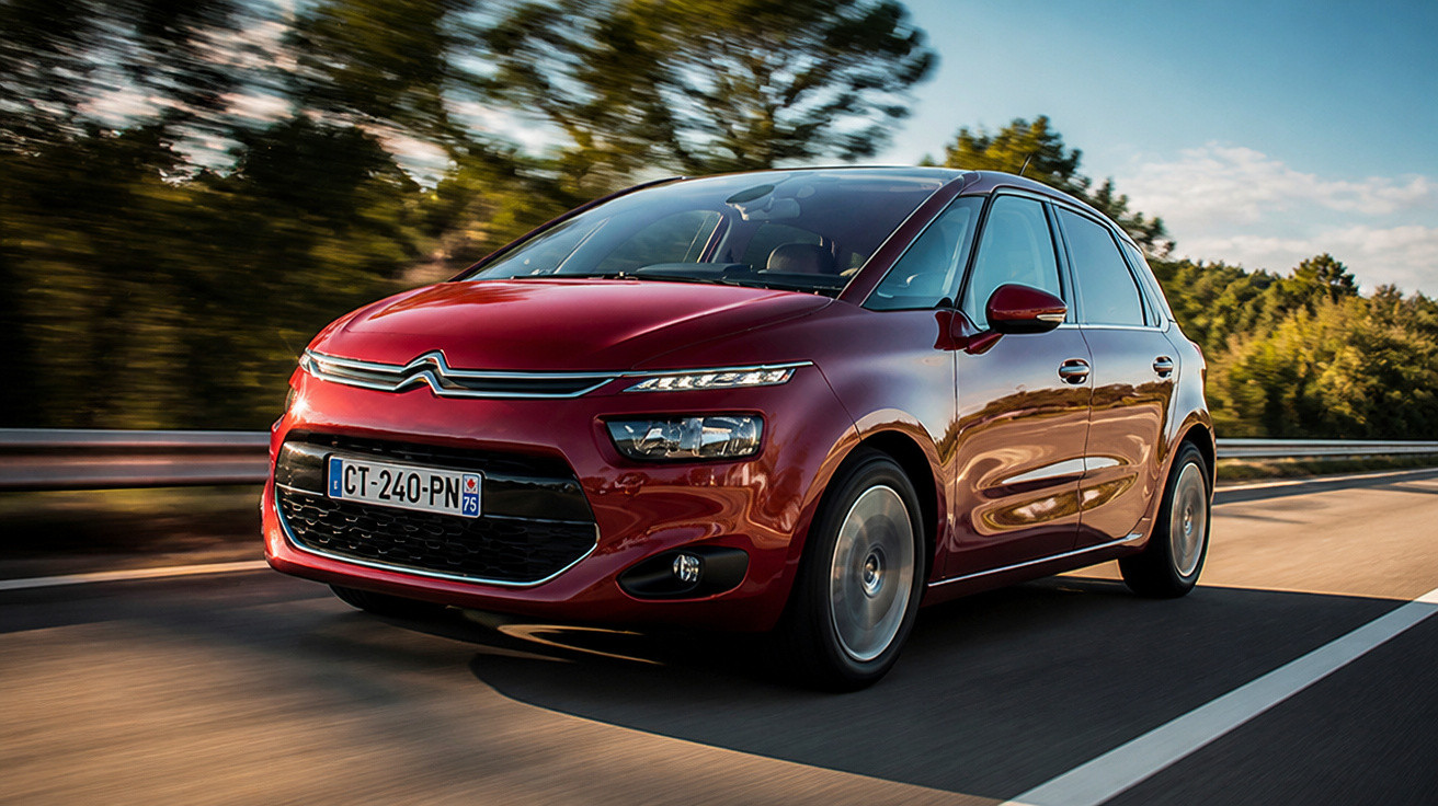 Carro Citroën vermelho a circular numa estrada rodeada de árvores em dia soalheiro.