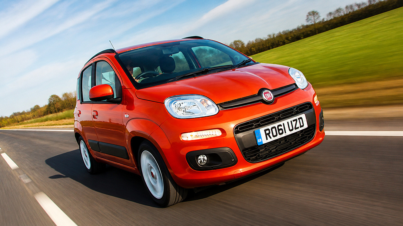 Carro Fiat Panda vermelho a circular numa estrada com relva e árvores ao fundo sob céu azul.