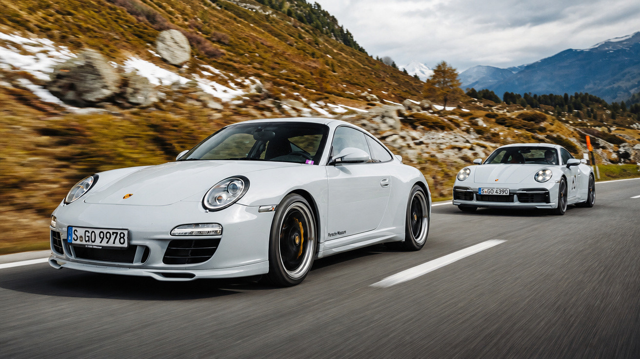 Dois carros Porsche brancos a circular numa estrada de montanha com céu nublado.