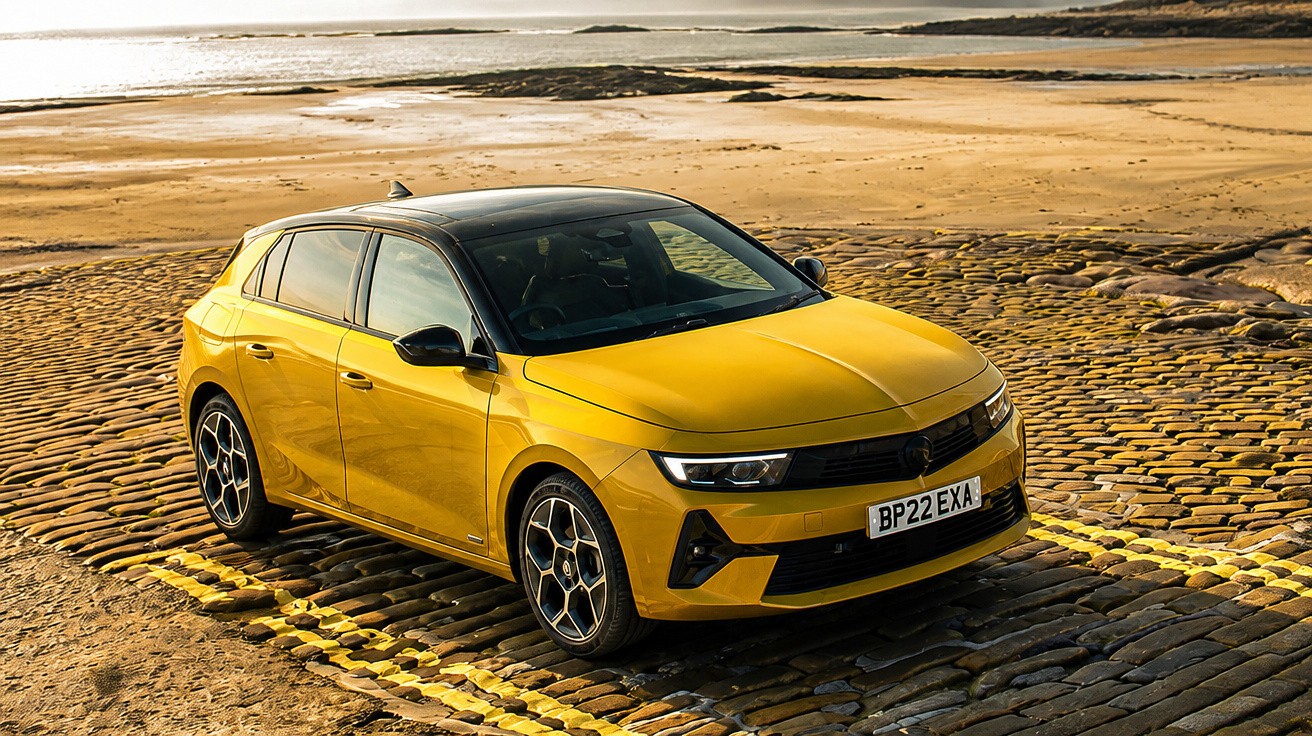 Carro amarelo estacionado em calçada de pedras com praia e mar ao fundo ao entardecer.