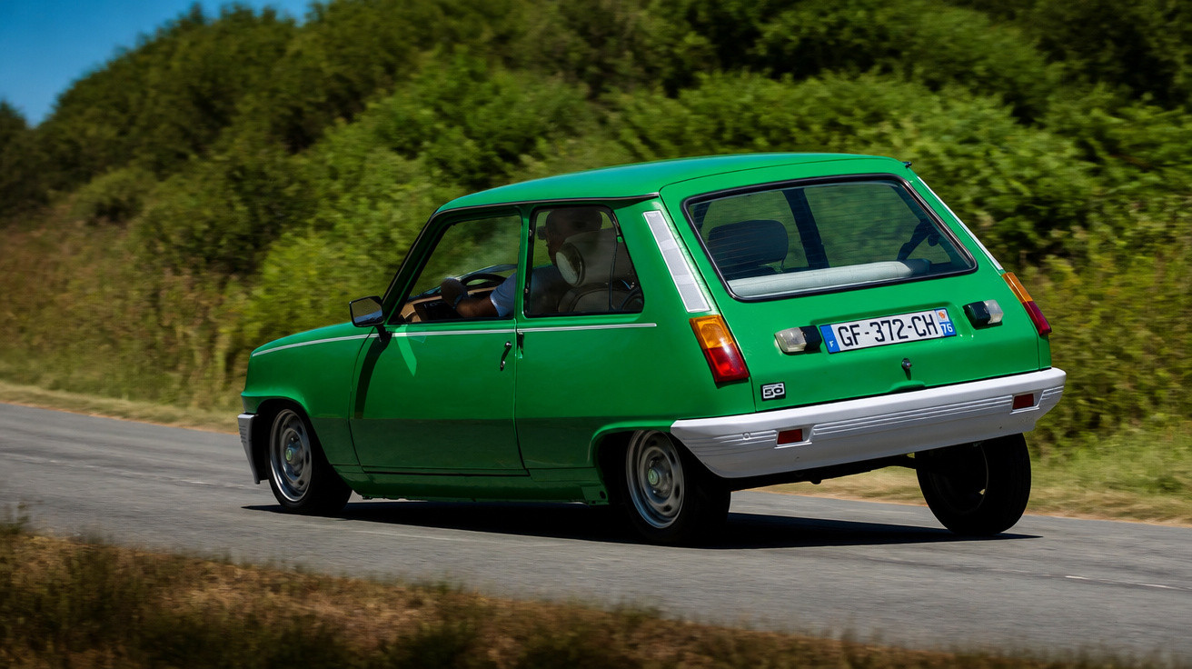 Carro clássico verde em movimento numa estrada rodeada de vegetação densa.