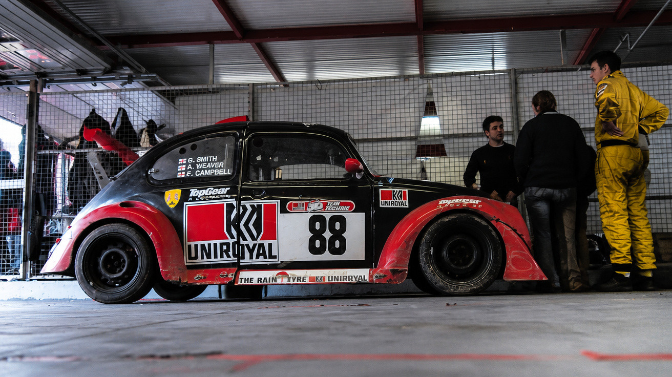 Carro de corrida clássico preto e vermelho com número 88 estacionado numa garagem com três homens ao lado.
