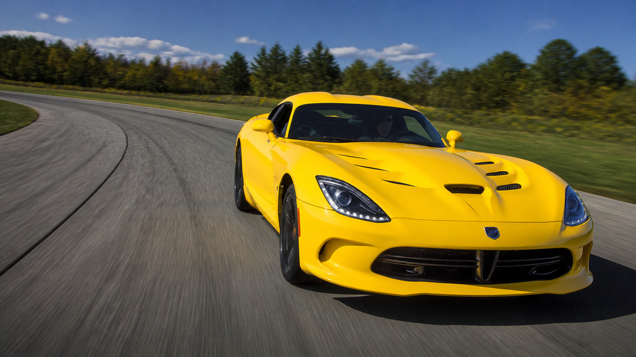 Carro desportivo amarelo a conduzir numa estrada sinuosa rodeada de árvores num dia solarengo.