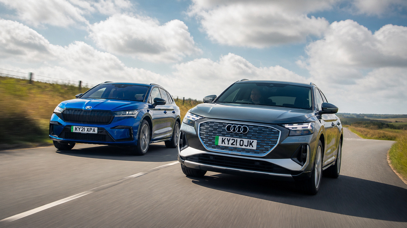 Dois carros elétricos, um Audi cinza e um Skoda azul, a circular numa estrada rural sob céu nublado.