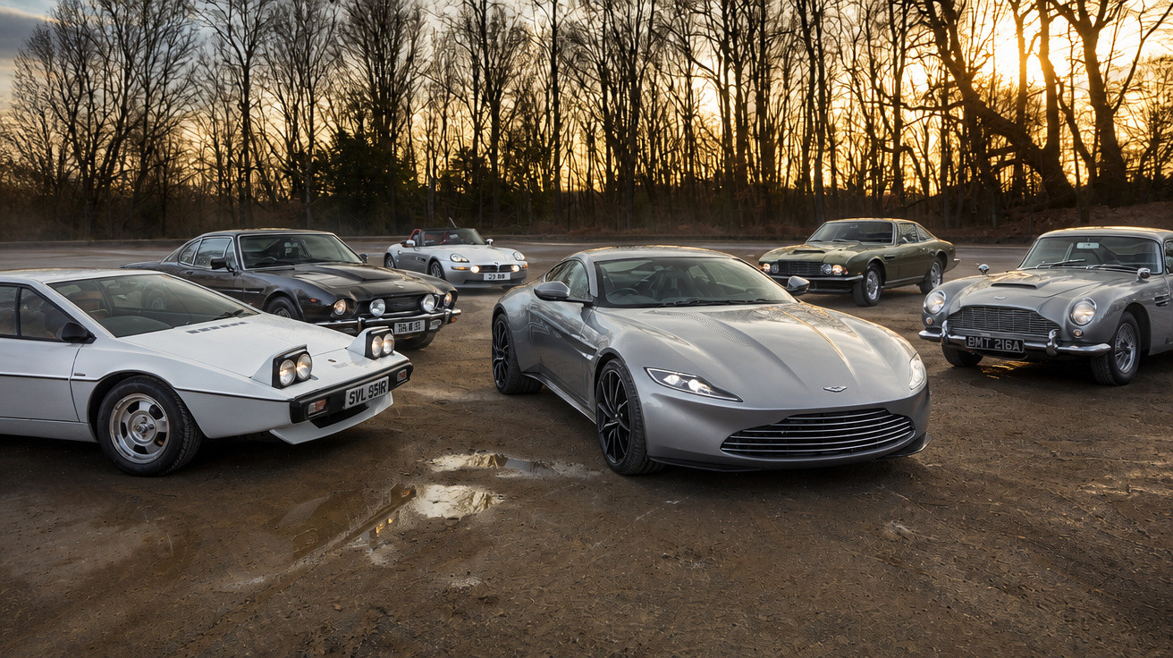Seis carros Aston Martin de diferentes épocas estacionados em terreno aberto ao pôr do sol.