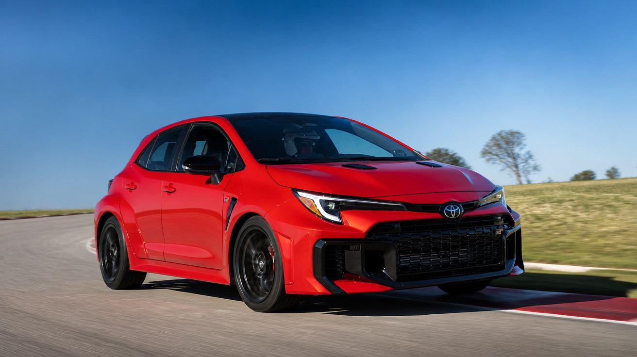 Carro desportivo Toyota vermelho a acelerar numa pista de corrida sob céu azul e campo ao fundo.