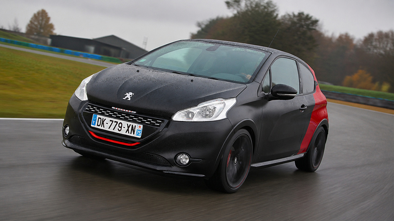 Peugeot 208 GTi preto com detalhes vermelhos circulando numa estrada molhada sob céu nublado.
