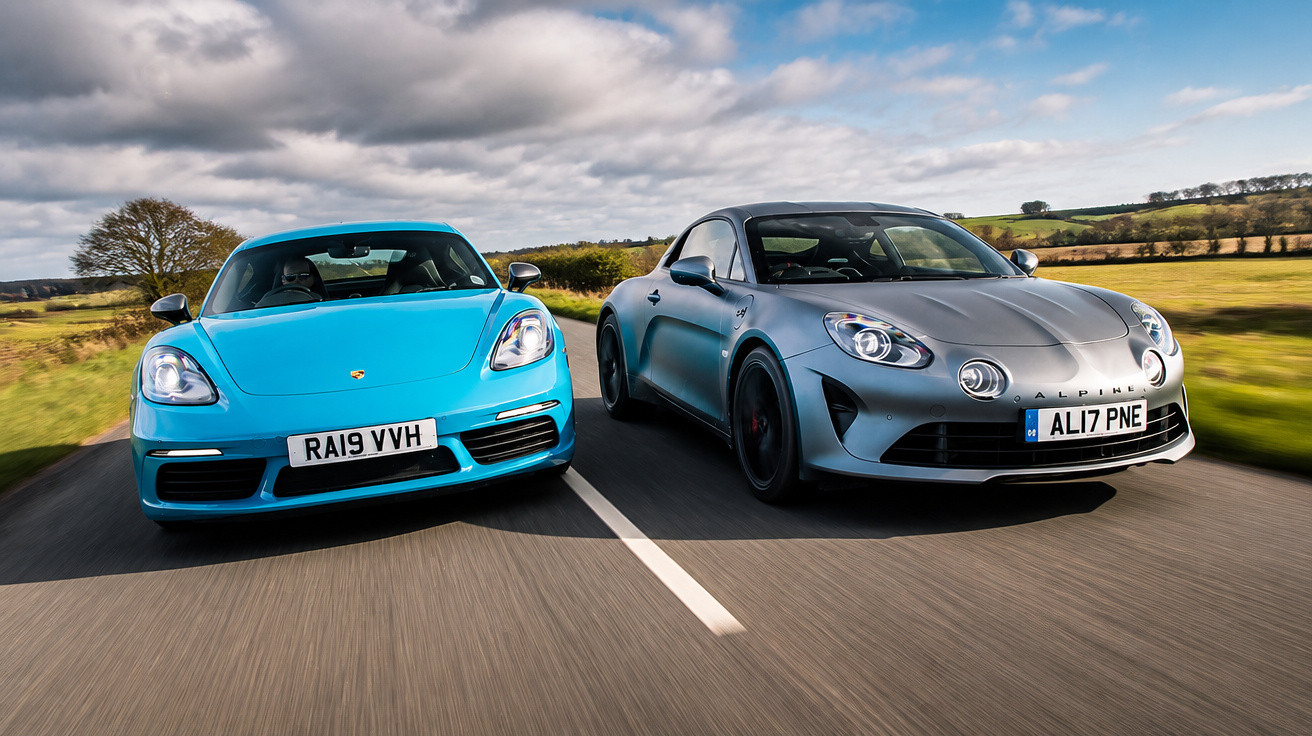 Dois carros desportivos, um azul Porsche e um cinzento Alpine, a circular numa estrada rural.