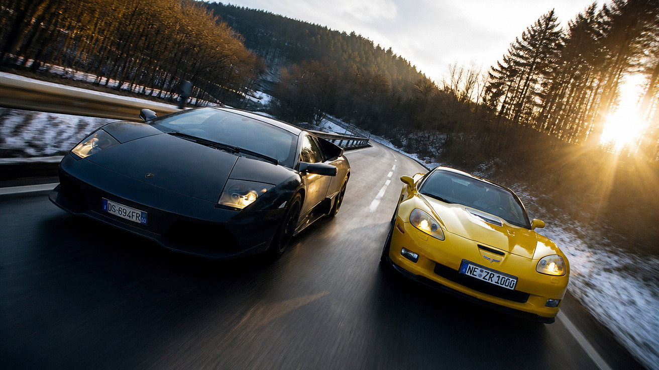 Dois carros desportivos, um preto e um amarelo, a circular numa estrada entre árvores com neve ao entardecer.