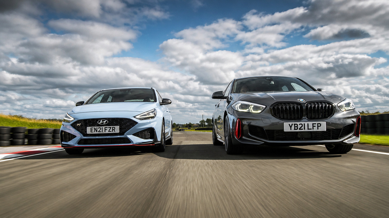 Dois carros desportivos, Hyundai azul e BMW preto, lado a lado numa pista de corridas sob céu nublado.
