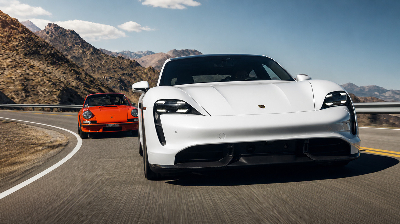 Dois carros Porsche, branco e vermelho, a conduzir numa estrada sinuosa entre montanhas.