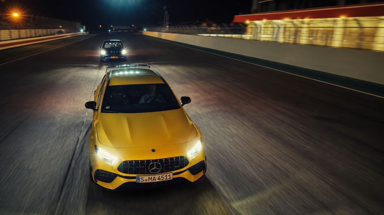 Carro desportivo amarelo Mercedes-Benz a conduzir de noite numa pista de corrida iluminada com outro carro atrás.