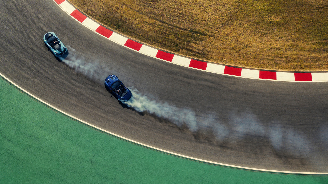 Dois carros desportivos azuis numa curva de circuito, com fumo a sair das rodas traseiras.
