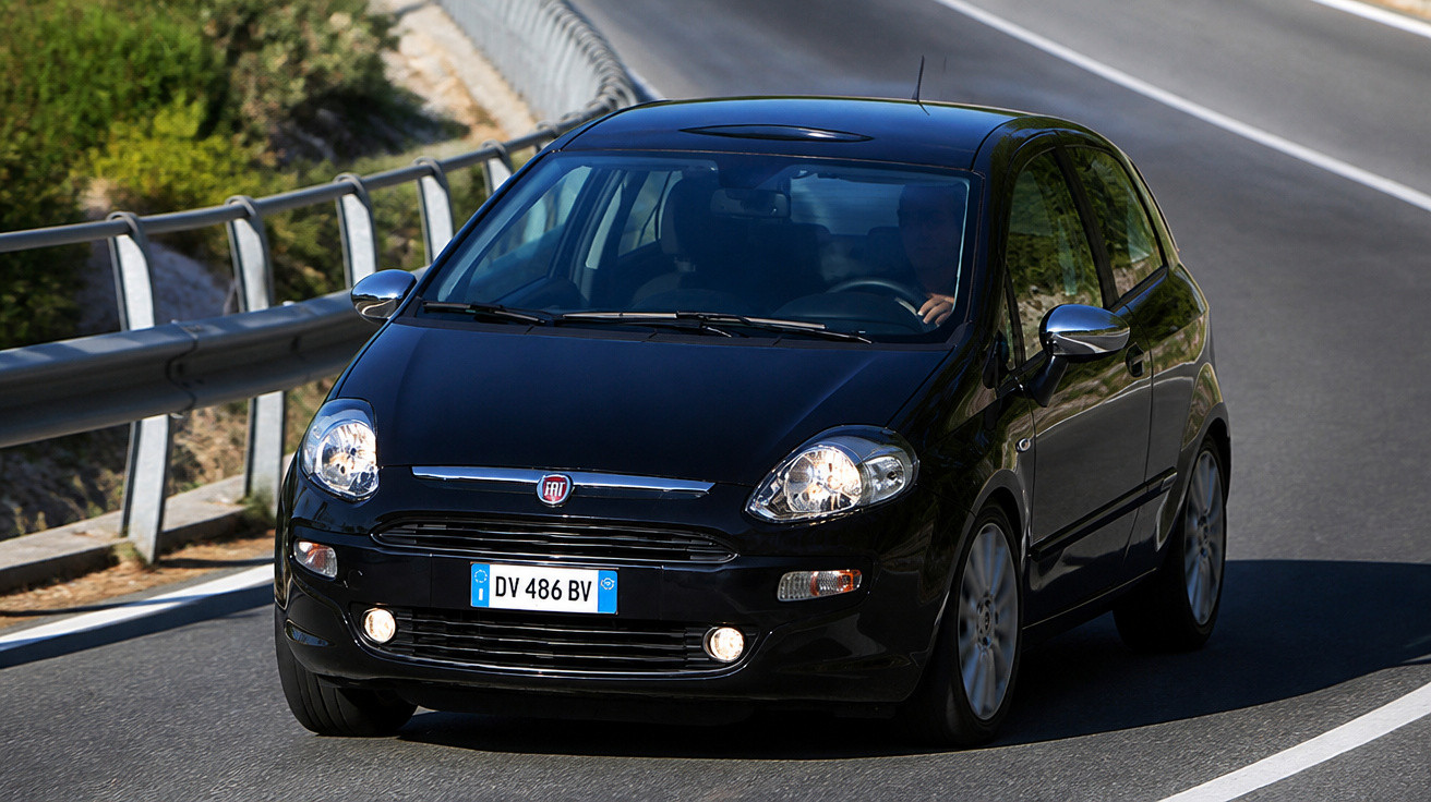 Carro preto Fiat a circular numa estrada com faixa branca e proteção metálica lateral.